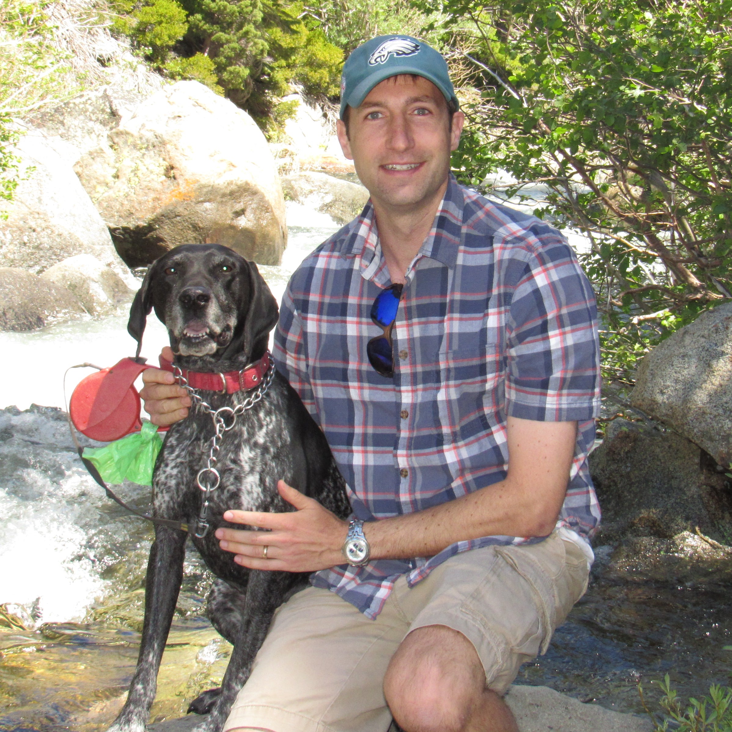 Photo of Peter Woodruff crouched next to a stream with his dog in the summer.