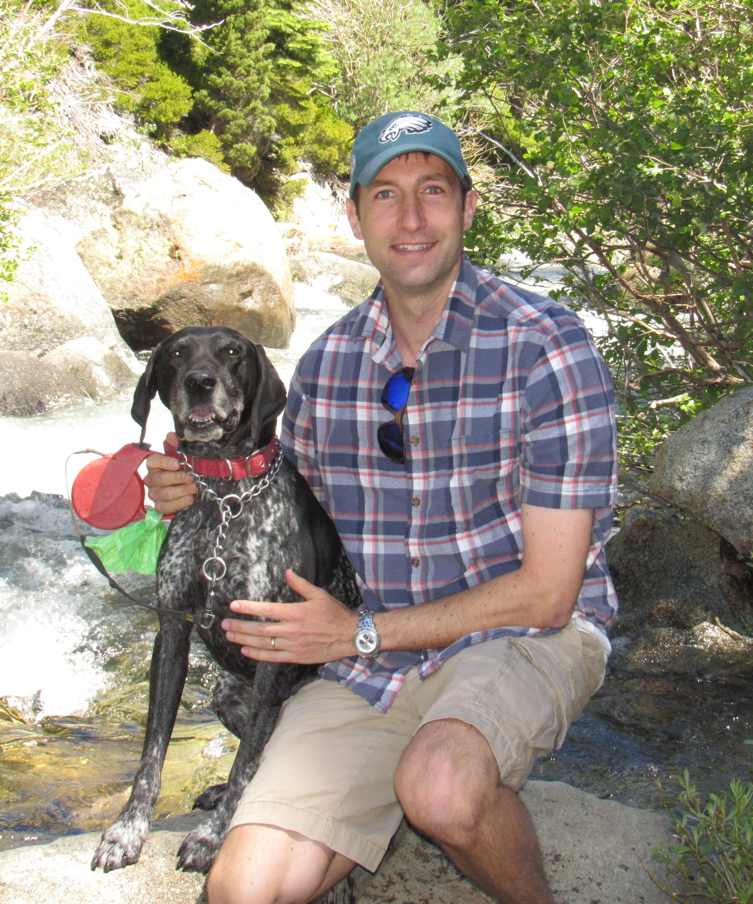 Photo of Peter Woodruff crouched next to a stream with his dog in the summer.